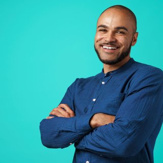 Man in blue shirt stands in front of a blue background and laughs