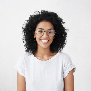 Woman with black curly hair stands in front of a white background and smiles