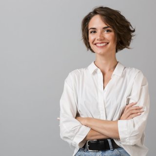 Woman with brown hair and white blouse stands in front of a gray background