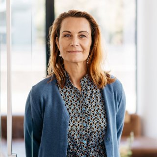 Woman with long brown hair stands in front of a glass wall and smiles